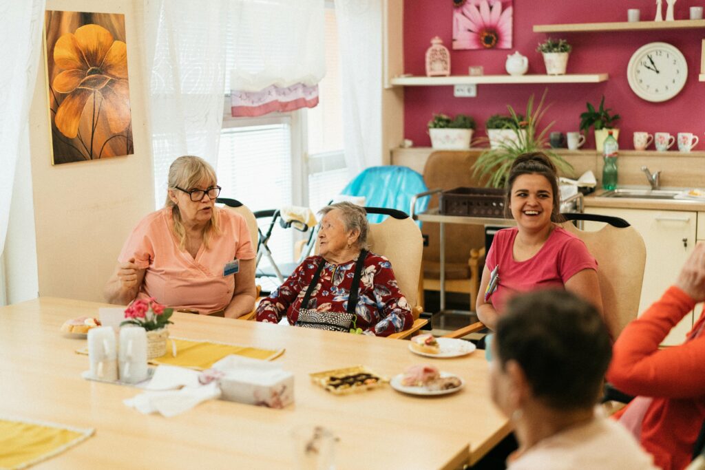 Elderly residents and caregivers enjoying a meal and conversation in a cheerful dining space